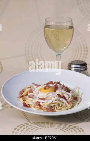 Teller mit Linguine mit Speck und Spiegelei und Glas Weißwein Stockfoto
