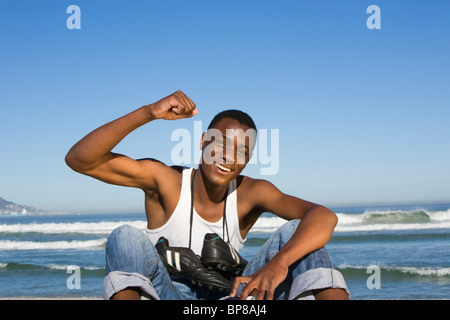 Mann, sitzend mit am Strand mit Fußballschuhe um seinen Hals jubeln Stockfoto