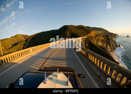Ein Auto mit einem Surfbrett auf Top Reisen über die Bixby Creek Bridge, auf dem Highway 1 in Big Sur, Kalifornien, USA. Stockfoto