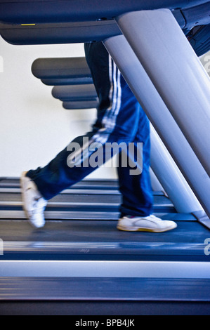 Nicht identifizierbare Beine mit lockeren Jogginghosen, die in einem Fitnessstudio auf einem Laufband laufen. Stockfoto