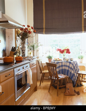 Alte hölzerne Stühle am Tisch mit blau + weiß aufgegebenes Tuch vor Erker mit dunkelgrau blind in Landhausküche Stockfoto