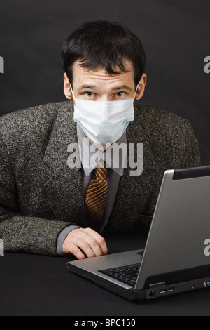 Der junge Mann in einer medizinischen Maske funktioniert im Internet Stockfoto