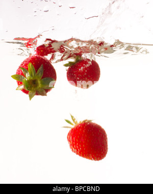Einige Erdbeeren fallen ins Wasser mit einem Schuss Stockfoto