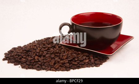 Eine Tasse Kaffee sitzen auf eine Untertasse auf einen Haufen von Kaffeebohnen. Stockfoto