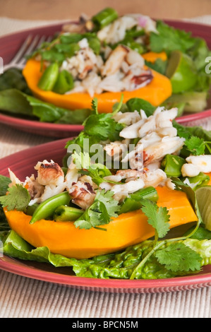 Papaya gefüllt mit Dungeness Krabbensalat, Zucker, Zuckerschoten und Koriander Beilage serviert auf einem Bett aus Römersalat. Stockfoto