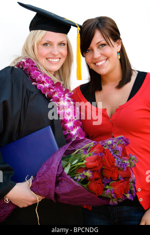 Ein Lächeln auf den Lippen Dipl.-Mütze und Mantel tragen Lei steht mit unterstützender Freund. Stockfoto