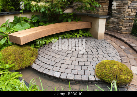 Gartenbank und steinernen Terrasse in kreisförmigen Kurven, mit Moos, Farn, Hecken, Wand Stockfoto