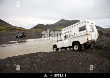 2 Land Rover fording eines Flusses in das innere Hochland von Island. Defender 90 und ein Defender 130 mit einem Wohnmobil Stockfoto