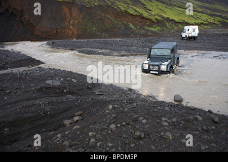 2 Land Rover fording eines Flusses in das innere Hochland von Island. Defender 90 und ein Defender 130 mit einem Wohnmobil Stockfoto