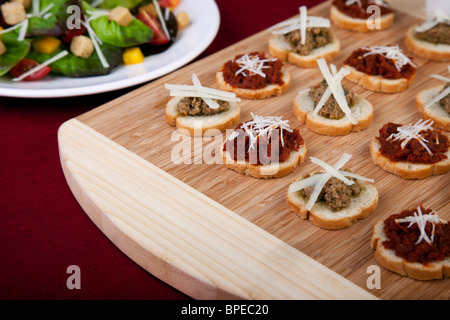 Frische hausgemachte sonnengetrocknete Tomaten Tapenade auf geröstetem Baguette belegt mit frisch geriebenem Käse und einem Beilagensalat. Stockfoto