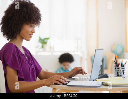 Mutter mit Kind im Hintergrund am Laptop arbeiten Stockfoto