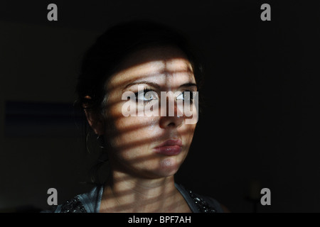 Junge attraktive Frau sitzt mit einer ernsten Stimmung oder Ausdruck und Linien der Schatten über Gesicht Stockfoto