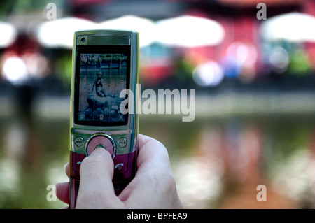 Eine Person, die ein Foto mit ihrer Handy-Kamera des Replikats "Kleine Meerjungfrau" in Tivoli Gardens, Copenhagen. Stockfoto