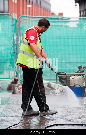 Arbeiter mit Jet Hochdruckreiniger um zu reinigen eine Baustelle in Hereford, Großbritannien. Mann mit Hochdruck Jetwash Wasserschlauch. Stockfoto