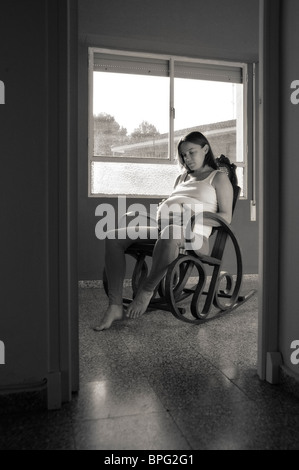 Schwangere Frau zu Hause, saß in einem Schaukelstuhl am Fenster Stockfoto