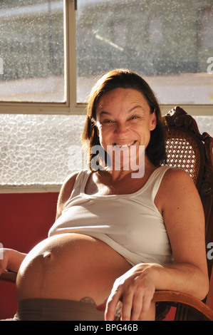 Schwangere Frau zu Hause, saß in einem Schaukelstuhl am Fenster Stockfoto