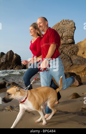 Mann und Frau mit Hund am Strand joggen. Stockfoto