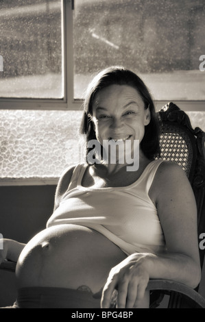 Schwangere Frau zu Hause, saß in einem Schaukelstuhl am Fenster Stockfoto