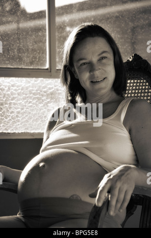 Schwangere Frau zu Hause, saß in einem Schaukelstuhl am Fenster Stockfoto