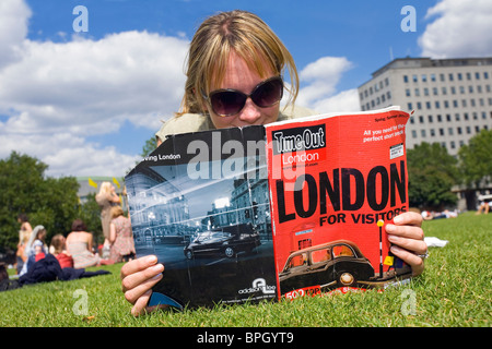 Frau liest eine Zeitschrift auf dem Rasen auf der South Bank in London Stockfoto