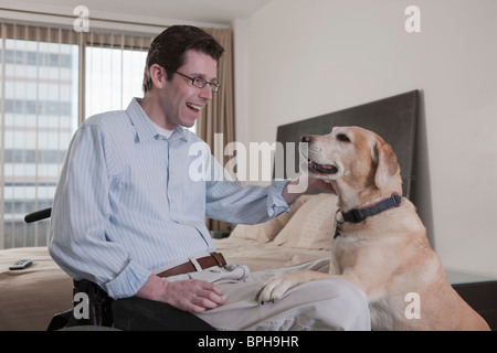 Mann in einem Rollstuhl mit einem Servicehund im Schlafzimmer spielen Stockfoto