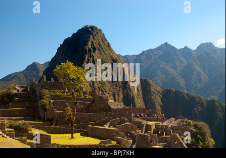 Touristen inmitten der komplizierten Steinarbeiten von zerstörten Gebäuden und Gartenterrassen an der alten Inka-Stadt Machu Picchu, Peru. Stockfoto