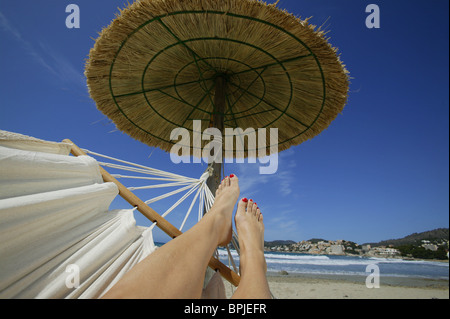 Womans Beine in einer Hängematte unter einem Strohdach Sonnensegel, Mallorca, Balearen, Spanien Stockfoto