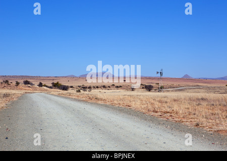 Unbefestigte Straße führt in die Landschaft-Szene mit Windmühle und Bergen im Hintergrund Stockfoto