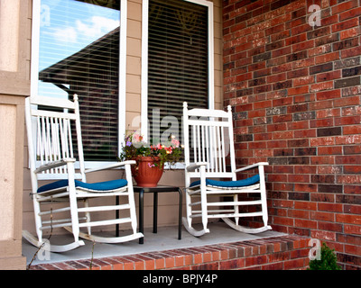 Zwei Schaukelstühlen sitzen auf der kleinen Veranda ein modernes Backsteinhaus. Stockfoto