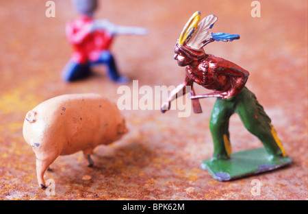 Nahaufnahme von zerkratzten Metall Blei Modelle der Native American Indian Bauernhof Schwein und rot-ummantelten Soldat mit dem Gewehr Ziel Stockfoto