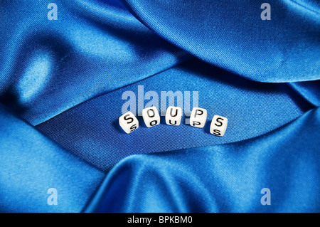 Royal Blue satin Hintergrund mit reichen Falten und Fältchen für Textur ist das Wort Suppen in schwarz / weiß Cube Schriftzug der Serie. Stockfoto