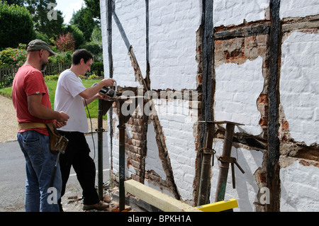 Renovierung einer alten Holz gerahmt denkmalgeschütztes Gebäude Arbeiter Ziegel vor dem Einbau des neuen Eichenbalken entfernen Stockfoto