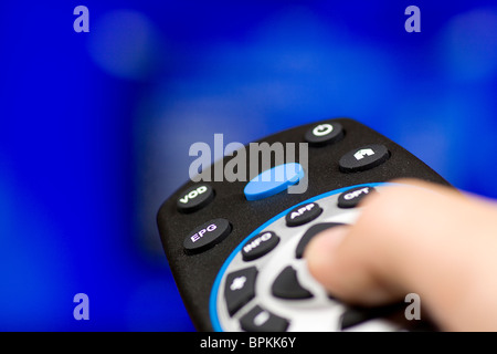 Hand, die TV-Fernbedienung mit einem Fernseher im Hintergrund. Hautnah. Stockfoto