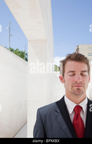 Junge Unternehmer mit Augen geschlossen vor urbaner Kulisse Stockfoto