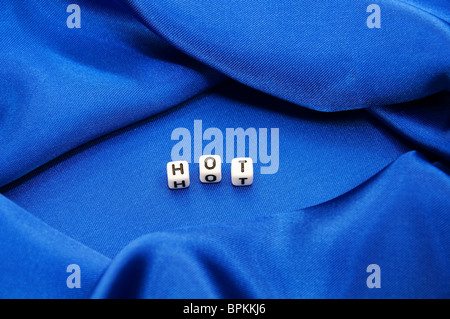 Royal Blue satin Hintergrund mit reichen Falten und Fältchen für Textur ist das Wort heiß in schwarz / weiß Cube Schriftzug der Serie. Stockfoto