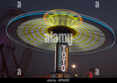 Die bunt beleuchteten Yo Yo dreht sich vor dem sanften Riesenrad am Nachthimmel an der New Jersey State Fair Stockfoto