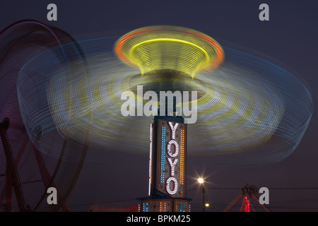 Die bunt beleuchteten Yo Yo dreht sich vor dem sanften Riesenrad am Nachthimmel an der New Jersey State Fair Stockfoto