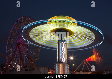 Die bunt beleuchteten Yo Yo dreht sich vor dem sanften Riesenrad am Nachthimmel an der New Jersey State Fair Stockfoto