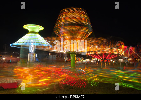 Bunt beleuchtete Fahrten mit dem Sizzler im Vordergrund, drehen gegen den Nachthimmel während der New Jersey State Fair Stockfoto