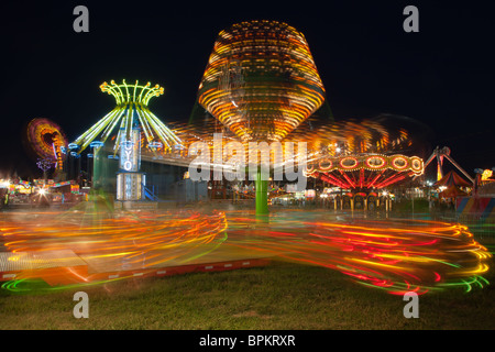 Bunt beleuchtete Fahrten mit dem Sizzler im Vordergrund, drehen gegen den Nachthimmel während der New Jersey State Fair Stockfoto