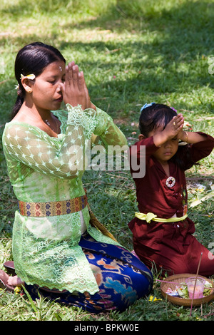 Eine Mutter und ihre Tochter sitzen mit Hände gefaltet im Gebet auf einer Rasenfläche in Bali Indonesien Stockfoto