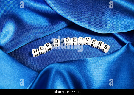 Royal Blue satin Hintergrund mit reichen Falten und Fältchen für Textur ist das Wort Hor d'oeuvers in schwarz / weiß Cube Schriftzug Stockfoto