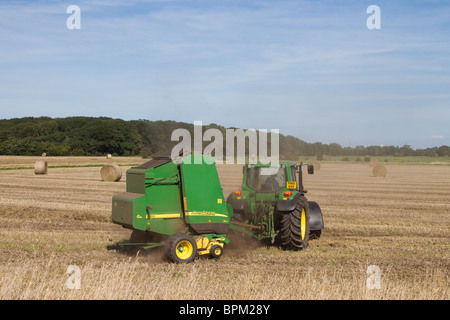 John Deere Ballenpressen, Rundballenpresse mit variabler Kammer. Ein Bauernhof. Traktortraktor Straw at Mere Brow, Hesketh Bank, Southport, Lancashire, Großbritannien Stockfoto