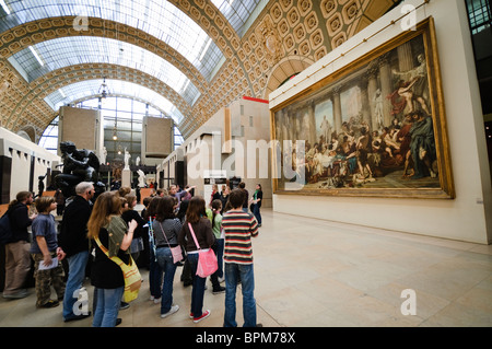 Musée d'Orsay Schulführung Schüler mit Guide Besichtigung von Gemälden im ehemaligen Bahnhof Paris Frankreich | PARIS, Frankreich – Eine Schulgruppe versammelt sich vor Thomas Coutures monumentalem Gemälde „die Römer der Dekadenz“ aus dem Jahr 1847 in der Haupthalle des Musée d'Orsay. Das Museum befindet sich im ehemaligen Gare d’Orsay, einem Bahnhof der Beaux-Arts, der 1900 für die Ausstellung Universelle gebaut wurde. Seine Bestände, die französische Kunst von 1848 bis 1914 umfassen, sind vor allem für impressionistische und post-impressionistische Werke bekannt. Stockfoto