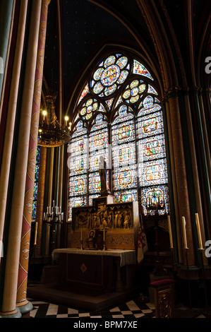 Notre-Dame de Paris Kapelle Buntglasfenster Altar Paris Frankreich // PARIS, Frankreich — Eine Kapelle im Inneren von Notre Dame de Paris verfügt über einen markanten Altar, der durch ein prächtiges Buntglasfenster beleuchtet wird. Das komplizierte gotische Buntglas, ein Wahrzeichen der Kathedrale, zeigt verschiedene religiöse Szenen und Figuren. Der reich verzierte Altar ist mit detaillierten Schnitzereien verziert, darunter ein Relief, das die Absetzung Christi darstellt, und wird von einer Statue gekrönt, die zum heiligen Raum beiträgt. Notre Dame de Paris, eine mittelalterliche katholische Kathedrale, ist ein bedeutendes Wahrzeichen im Herzen von Paris, Île-de-France, Franc Stockfoto