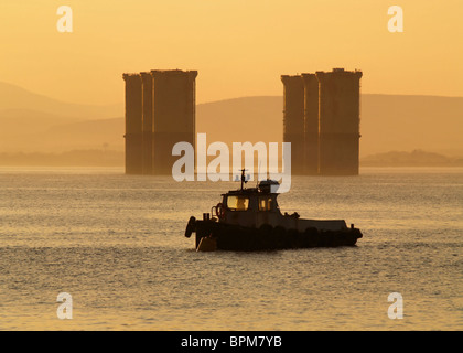 Ein Workboat liegt neben den Beinen einer Nordsee-Öl-Plattform wie die Sonne über den Cromarty Firth, Schottland. Stockfoto