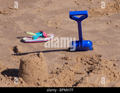 Des Kindes Sandale, Spaten und Sandburg auf einem Sandstrand, Clacton, UK Stockfoto