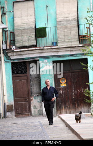 Man Walking Dog – Ein Block von armen Häusern und Wohnungen Straßenszene von Olot in der La Garrotxa Comarca der Provinz Girona Katalonien in Spanien Stockfoto