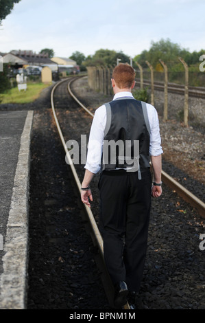 junge weiße männliche Zauberer mit Ingwer Haar außerhalb zu Fuß auf stillgelegten Bahngleisen Stockfoto