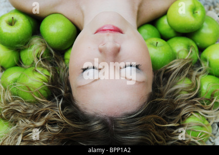 schöne junge weiße Frau im Bett von grünen Äpfeln Stockfoto
